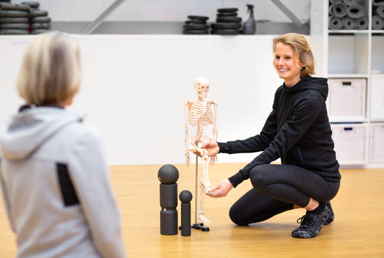 Personalcoach Lisa Stanke erklärt einer Kundin anhand eines Skelettmodells die menschliche Anatomie für das Schmerzcoaching