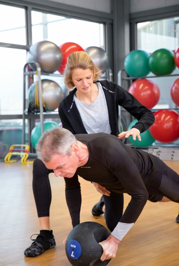 Personalcoach Lisa hilft einem Sportler bei der richtigen Ausführung einer Liegestützvariation